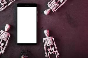 Skeletons around a smartphone with a white display on a dark background. photo