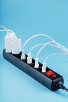 Black surge protector with a red button and connected white wires of electrical appliances on a blue background. photo