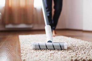 A cordless vacuum cleaner cleans the carpet in the living room with the bottom of the legs. Modern technologies for cleaning the house photo