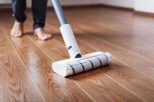 Human legs and a white turbo brush of a cordless vacuum cleaner cleans the parquet in the house. photo