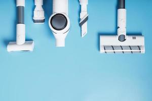 A set of nozzles and a white cordless vacuum cleaner in a row on a blue background, free space. Top view photo