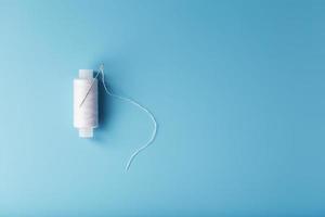 A skein of white thread with a needle on a blue background photo