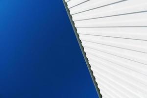 Textured white metal structures diagonally against a blue sky. photo