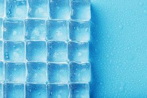 Ice cubes with water drops scattered on a blue background, top view. photo