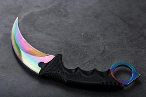 Kerambit dagger with a rainbow-colored blade on a dark textured background. photo