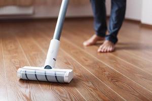 Human legs and a white turbo brush of a cordless vacuum cleaner cleans the parquet in the house. photo