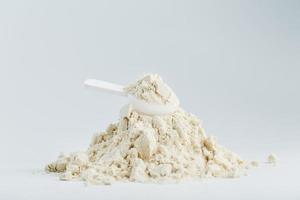 A mountain of soy protein isolate in powder with a measuring spoon on a white background. photo