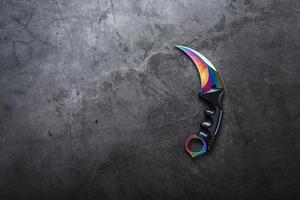 Kerambit dagger with a rainbow-colored blade on a dark textured background. photo