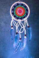 Dreamcatcher with multicolored weaving in blue smoke isolated on black photo