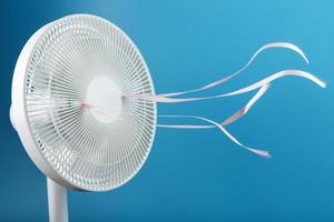 The electric fan is white with pink ribbons fluttering in the wind on a blue background photo