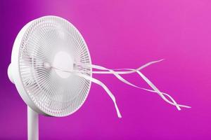 The electric fan is white with pink ribbons fluttering in the wind on a pink background. photo