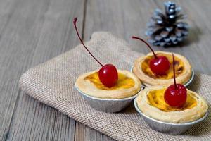 tarta de huevo en taza de papel de aluminio con cereza roja sobre mesa de madera foto