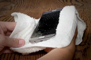 closeup Hands holding White cloth with wet smart phone drops on wooden floor photo