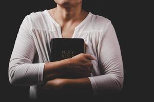 christian woman hand on holy bible are pray and worship for thank god in church with black background, concept for faith, spirituality and religion photo