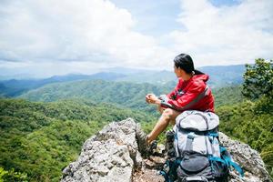 Young person hiking female sitting on top rock, Backpack woman looking at beautiful mountain valley at sunlight in summer, Landscape with sport girl, high hills, forest, sky. Travel and tourism. photo