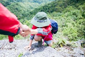 persona camina amigos ayudándose unos a otros a subir una montaña. hombre y mujer dando una mano amiga y un estilo de vida activo. una pareja de asia que camina se ayuda mutuamente. concepto de amistad mentor, trabajo en equipo. foto