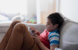 School kid using tablet readying story from internet, Happy boy sitting on sofa doing studying online learning  at home, Child holding digital pad using wifi playing game or chatting with friends. photo