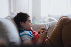 School kid using tablet readying story from internet, Happy boy sitting on sofa doing studying online learning  at home, Child holding digital pad using wifi playing game or chatting with friends. photo