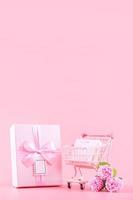 Mother's Day holiday gift design concept, pink carnation flower bouquet with wrapped box, shopping cart, bag, isolated on light pink background, copy space. photo