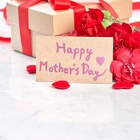 Mother's Day gift background, red carnation flower bouquet with wrapped kraft gift tied with ribbon isolated on marble white background, close up. photo