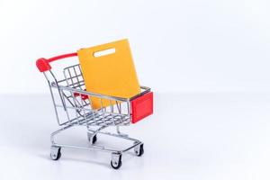 Shopping bags in a silver red shopping cart isolated on white table background, concept of staying home order, close up, copy space design. photo