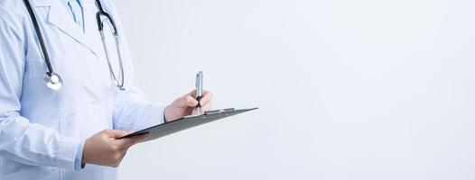 Doctor with stethoscope in white coat holding clipboard, writing medical record diagnosis, isolated on white background, close up, cropped view. photo