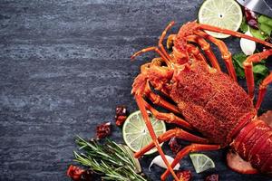 Cooked boiled lobster, delicious dinner seafood meal set with knife and fork on black stone slate background, restaurant menu design, top view, overhead photo