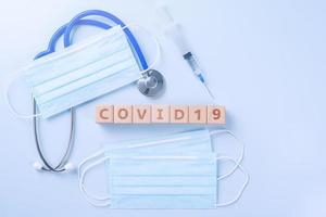 covid-19 palabra cubo de madera con máscara, equipo médico, concepto de prevención e infección pandémica de enfermedades mundiales, vista superior, plano, diseño superior foto