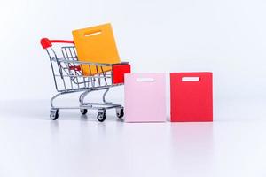 bolsas de compras en un carrito de compras rojo plateado aislado en el fondo de la mesa blanca, concepto de permanecer en casa, cerrar, copiar el diseño del espacio. foto