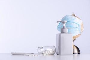 Concept of coronavirus COVID-19 pandemic to the world. Globe with face mask, sanitizer, medicine, clinical thermometer isolated on gray background, close up. photo