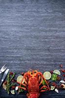 Cooked boiled lobster, delicious dinner seafood meal set with knife and fork on black stone slate background, restaurant menu design, top view, overhead