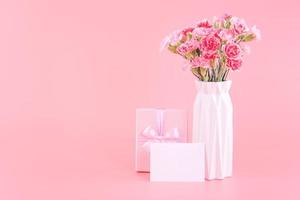 concepto de diseño de regalo de vacaciones del día de la madre, ramo de flores de clavel rosa con tarjeta de felicitación, aislado en fondo rosa claro, espacio de copia.