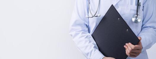 Doctor with stethoscope in white coat holding clipboard, writing medical record diagnosis, isolated on white background, close up, cropped view. photo