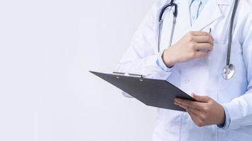 médico con estetoscopio en bata blanca sosteniendo portapapeles, escribiendo diagnóstico de registros médicos, aislado en fondo blanco, primer plano, vista recortada. foto