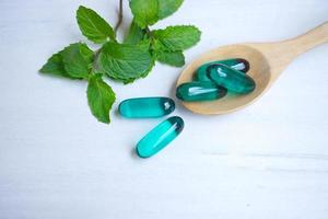 Blue capsules in wooden spoon with mint leaves on white wood background. photo