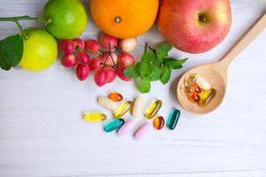 Multivitamin supplements from fruit on white wooden background photo
