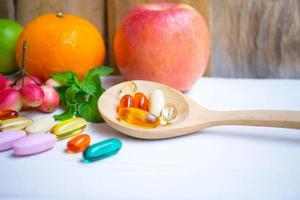 pastillas y cápsulas en cuchara de madera con frutas frescas.vitaminas y suplemento del concepto de frutas. foto