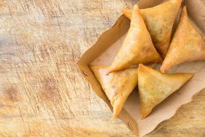 Samosas on brown papaer tray on rustic wood.Top view. photo