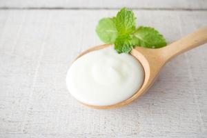 yogur blanco con hoja de menta en cuchara de madera sobre fondo de madera blanca. foto