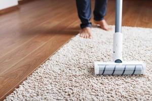 Human legs and a white turbo brush of a cordless vacuum cleaner cleans the carpet in the house photo