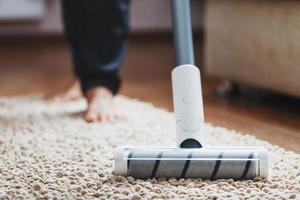 piernas humanas y un cepillo turbo blanco de una aspiradora inalámbrica limpia la alfombra de la casa foto