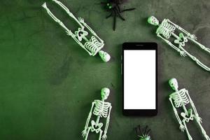 esqueletos alrededor de un teléfono inteligente con una pantalla blanca sobre un fondo oscuro. foto