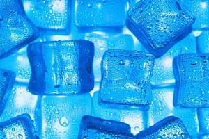 Ice cubes with water drops scattered on a blue background, top view. photo