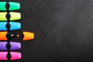 Multi-colored markers in a row on a black background, top view. photo