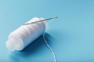 A skein of white thread with a needle on a blue background photo