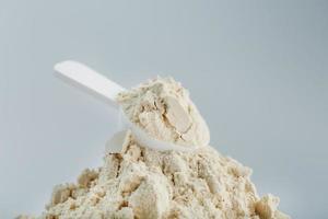A pile of protein powder with a measuring spoon on a white background. photo