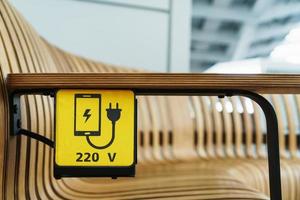 A socket with a device charging sign on a wooden bench at the airport. photo