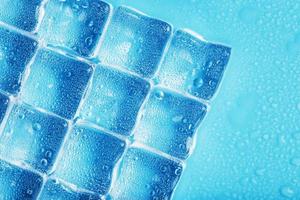 Ice made of cubes lined up with drops on a blue background photo