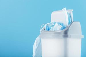 Waste bin full of used protective masks on a light blue background with free space. photo