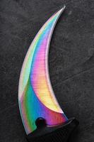 The sharp blade of the Kerambit knife made of steel is multicolored in close-up on a dark background. photo